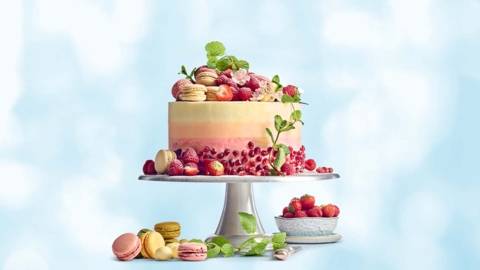 Witte chocoladetaart met frambozen, versierd met vers rood fruit, macarons en bloemen